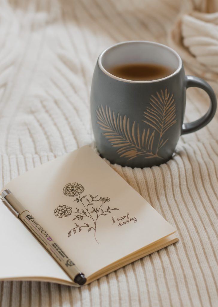Auf dem Bild ist ein Buch mit einer Zeichnung und einer Tasse Kaffee zu sehen.