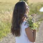 Frau mit Blumenstrauss schaut zur Sonne und denkt an ihr Coaching für Mamas in München